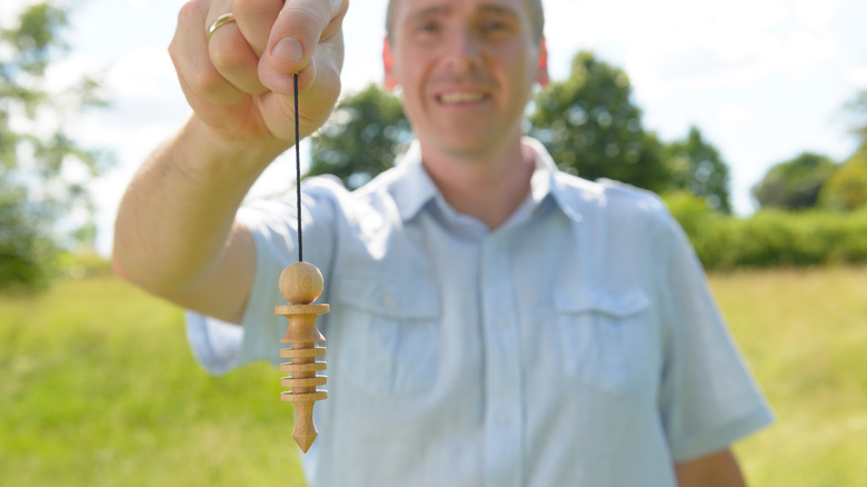 man holding dowsing pendulum outside