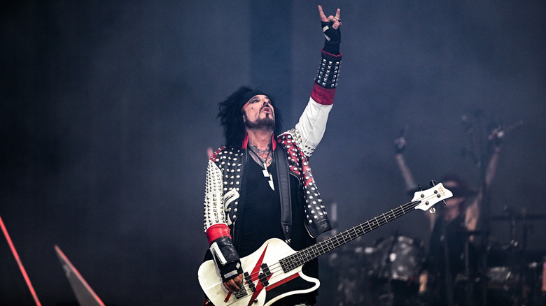 Nikki Sixx playing white bass guitar hand raised devil horns