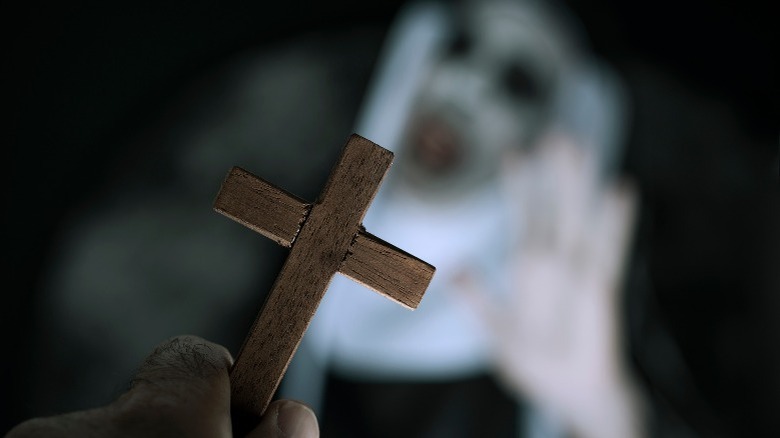 Hand holding a wooden cross at an evil nun