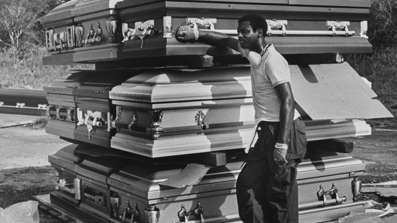 Man leaning against stack of unused caskets at Jonestown