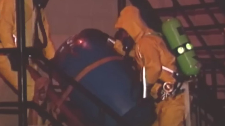 Person in hazmat suit carrying barrel