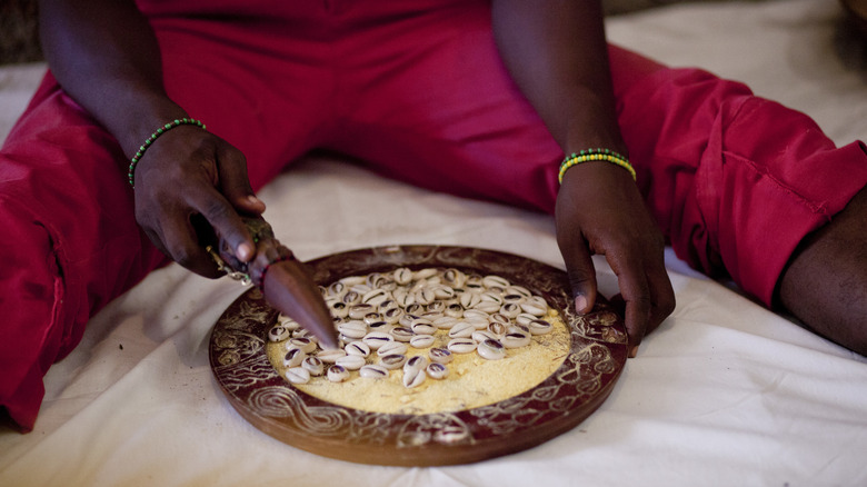 man reading cowrie shells holds wooden instrument