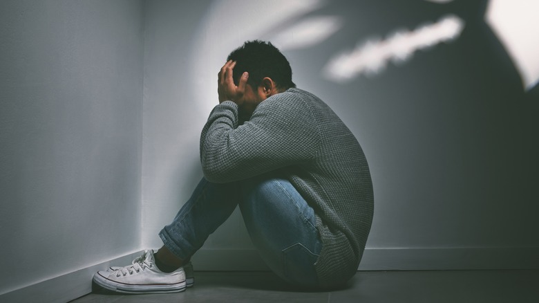 man covering face sitting in corner shadows