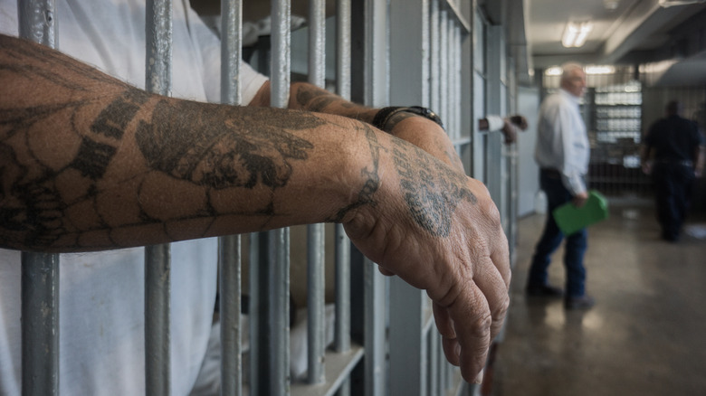 Man's tattooed arms hanging over prison bars