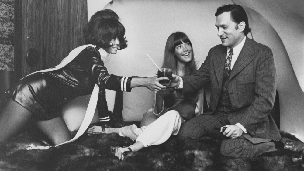 Hugh Hefner and two girls having a toast on a bed