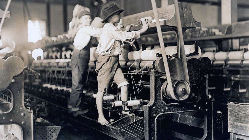 Two small boys in a  cotton mill fix a loom