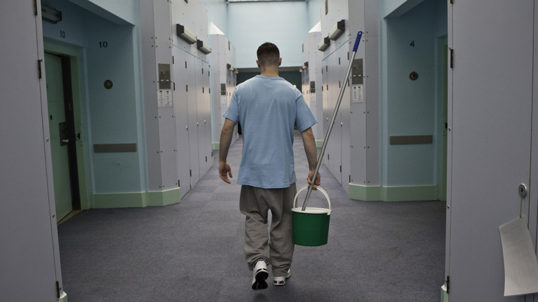 Prisoner with mop and bucket walking down hallway