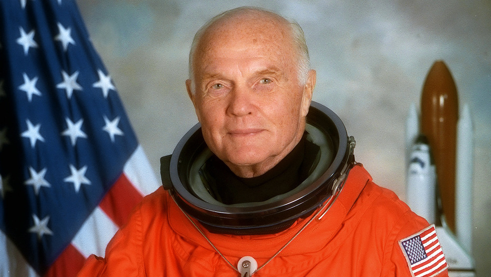 John Glenn in space suit in front of flag