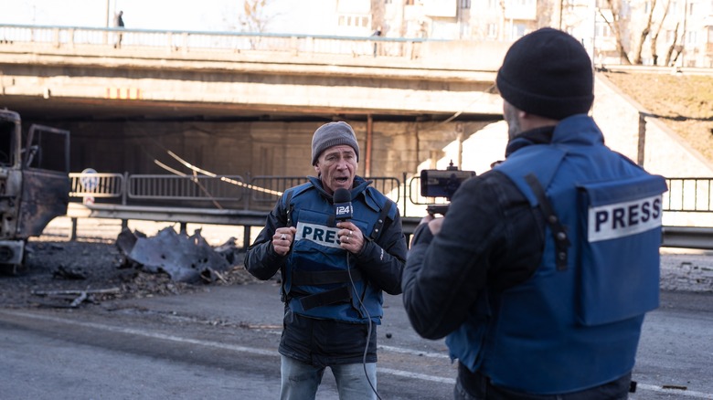 an Israeli film crew filming a report in Kyiv n Pobedy Avenue near a burned-out truck