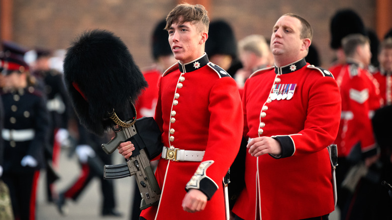 Guardsman carrying rifle with fur hat on end