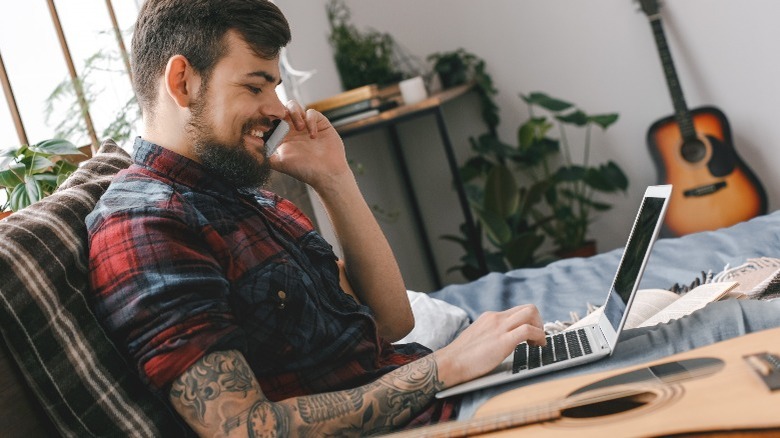 Musician on the phone with a laptop next to a guitar