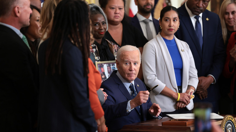 Joe Biden lifts pen while surrounded by staff