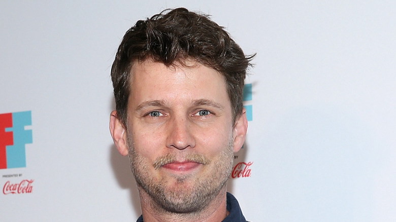 jon heder grimacing in front of a walmart ad wall at an event