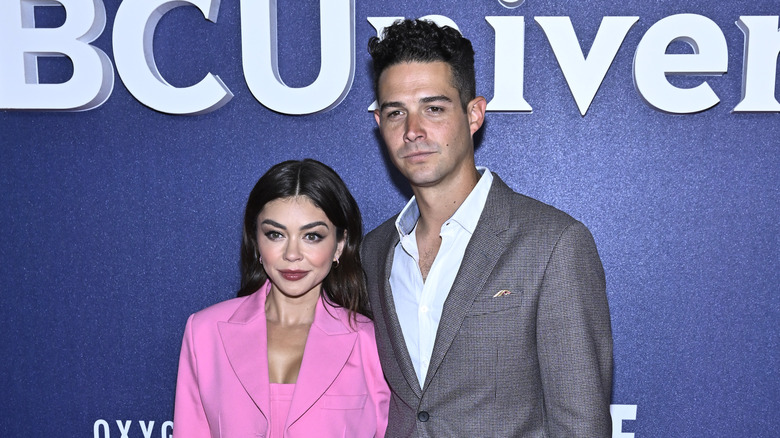 Sarah Hyland and husband Wells Adams posing in front of NBCUniversal logo