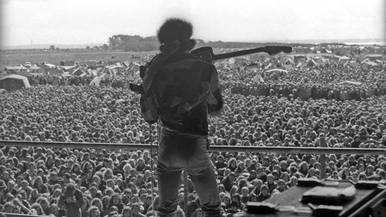 Jimi Hendrix from behind, play for a massive field of people