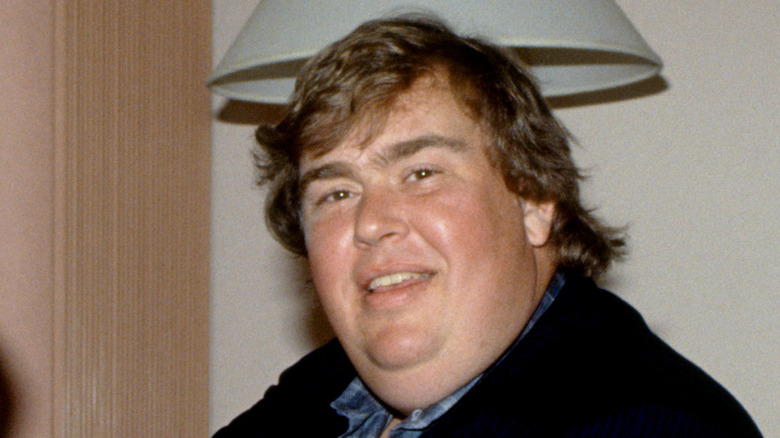 John Candy standing in front of a lamp smiling