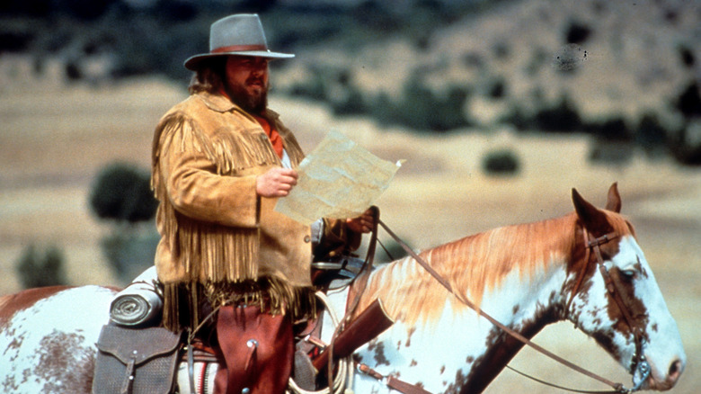 John Candy reading a map on horseback in a scene from Wagons East