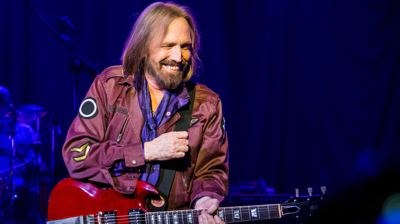 Tom Petty smiling and holding a red guitar while performing on stage