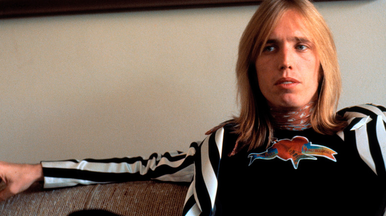 Tom Petty sits on a couch and looks away from the camera