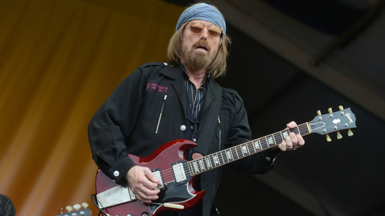 Tom Petty plays a red guitar on stage while wearing sunglasses and a blue bandana