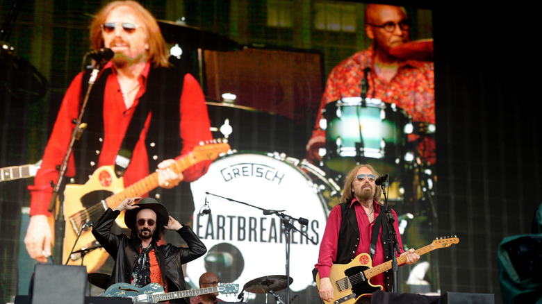 Mike Campbell and Tom Petty on stage while Petty and Steve Ferrone are projected on the screen behind the stage