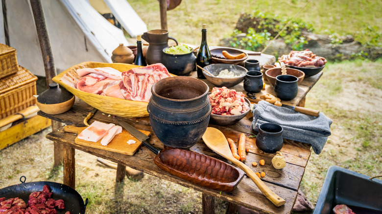 Raw meat, homemade food and pottery on the table at Viking historical reenactment