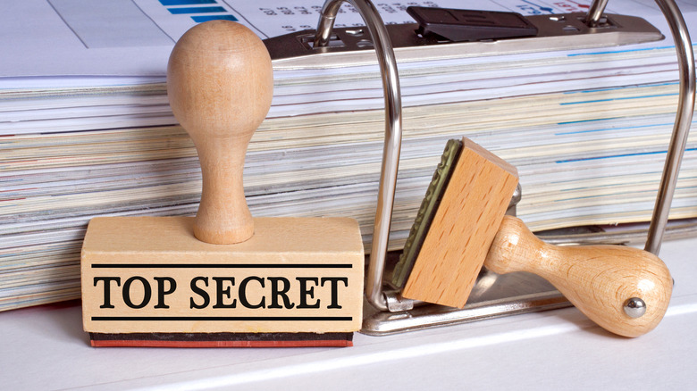 A "top secret" rubber stamp next to a binder of papers.