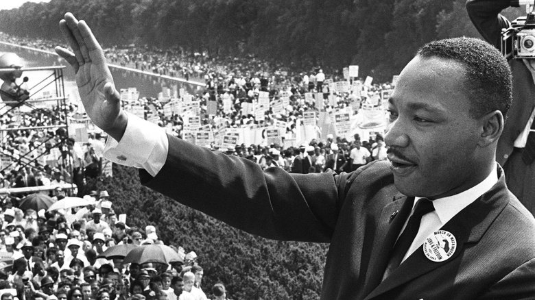 Martin Luther King Jr. in suit waving to crowd outside