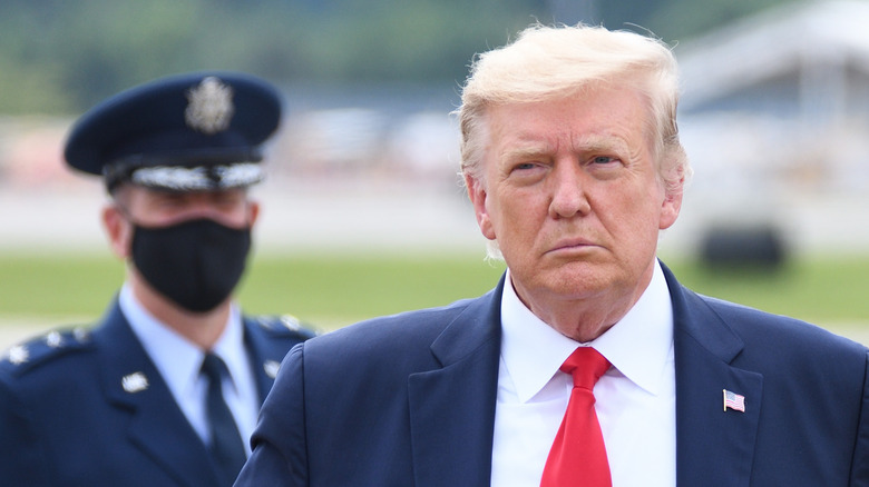 A masked official follows Donald Trump