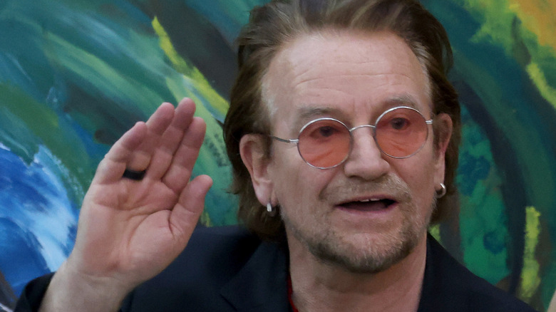 Bono in pink sunglasses waving blue wavy background