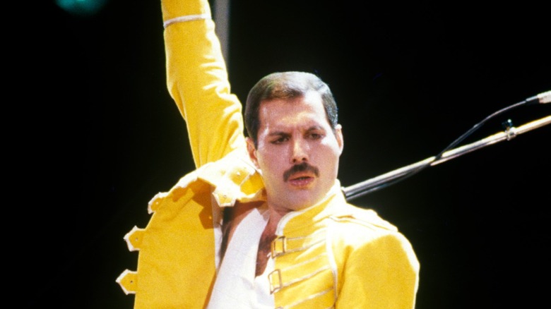 Freddie Mercury on stage in white vest and yellow jacket