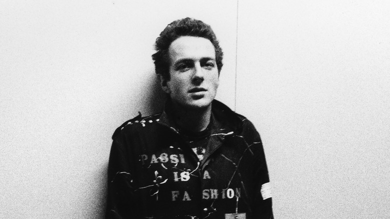 Joe Strummer in leather jacket with studs standing against a white wall