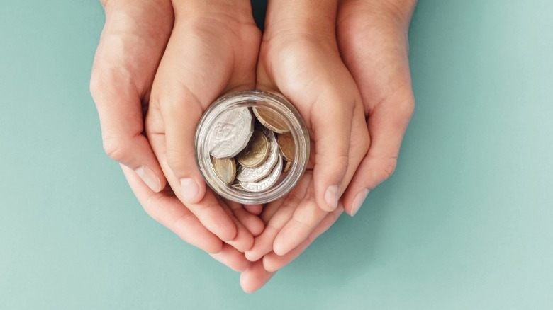 Hands clasping hands with coins in jar