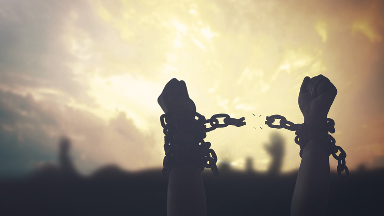 Silhouette human hands raising and broken chains at sunset background