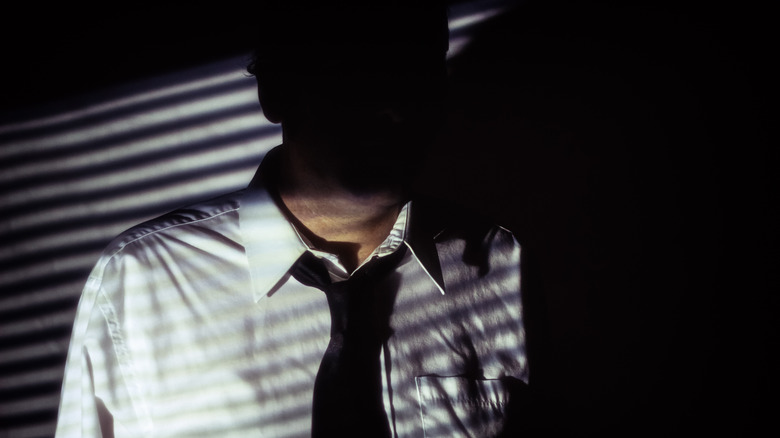 man in white shirt and black tie, face hidden by shadows