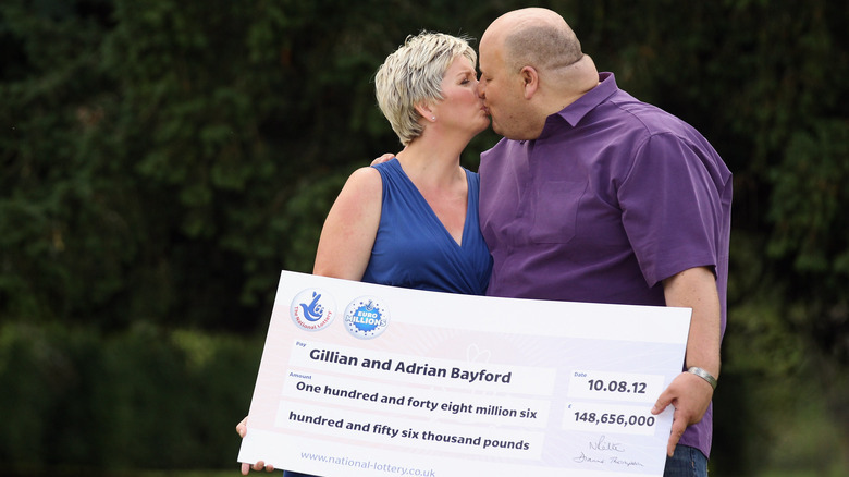 Adrian and Gillian Bayford holding giant lottery check kissing