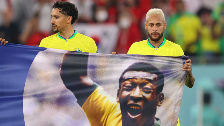 Two Brazilian World Cup players hold up banner of Pelé on pitch