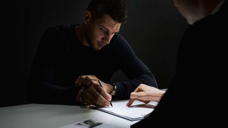 handcuffed man signing document