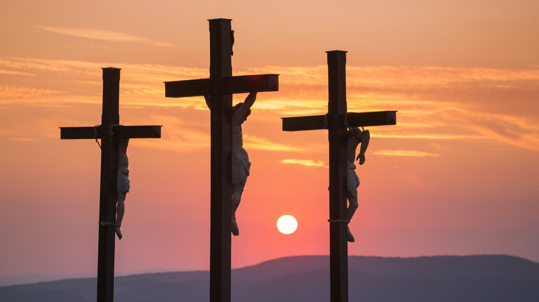 Three crosses with victims silhouetted against sunset