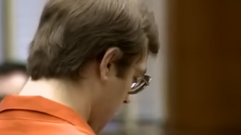 Jeffrey Dahmer downcast in jumpsuit and glasses