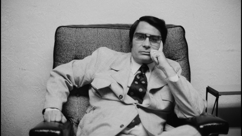 Jim Jones slouching in chair in suit