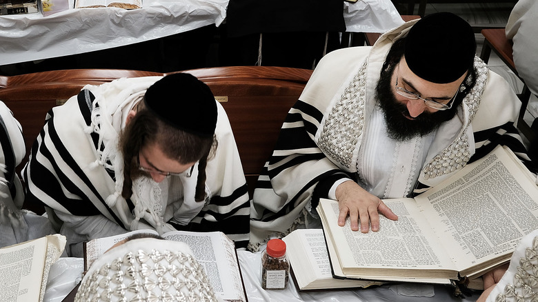 Orthodox Jews in white read Torah