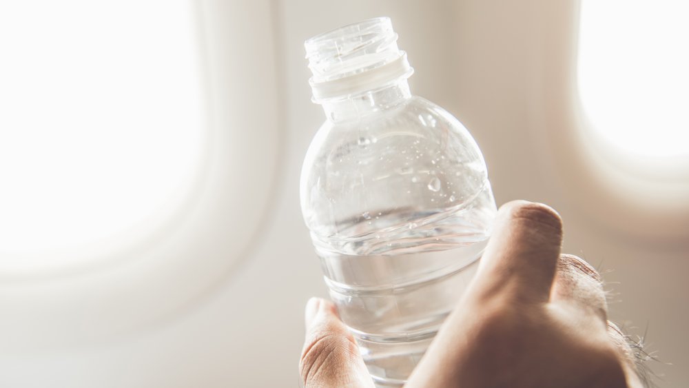 Hand holding water bottle by plane windows